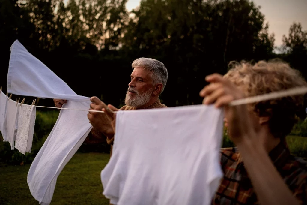 Mann hängt frisch gewaschene weiße T-Shirts zum Trocknen auf eine Wäscheleine.