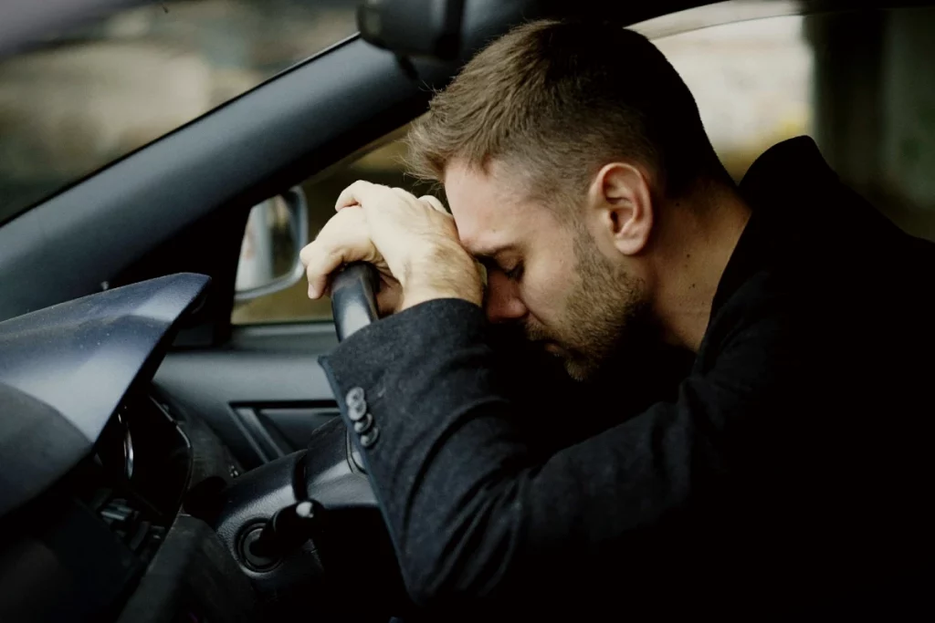 Mann sitzt erschöpft in seinem Auto und stützt traurig den Kopf auf das Lenkrad.