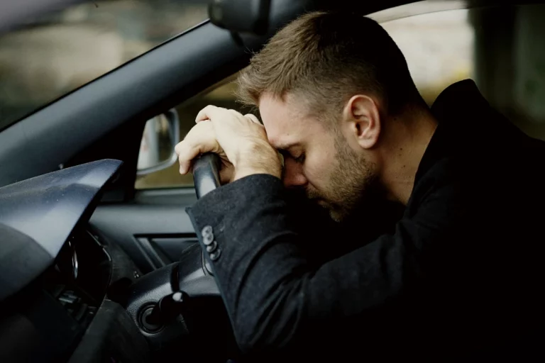 Mann sitzt erschöpft in seinem Auto und stützt traurig den Kopf auf das Lenkrad.