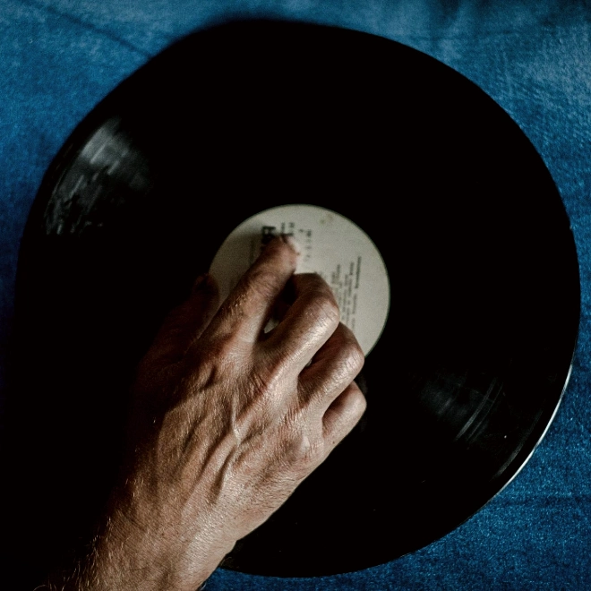 Männerhand legt eine schwarze Vinylschallplatte auf einen blauen Untergrund.