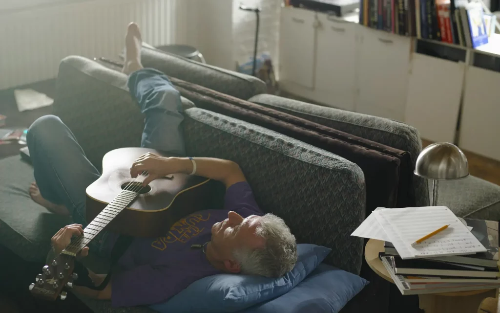 Mann entspannt mit einer Gitarre im Wohnzimmer – Hobbys schaffen Ausgleich zum Alltag und fördern die mentale Erholung.