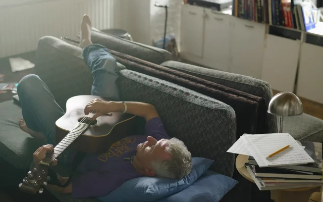 Mann entspannt mit einer Gitarre im Wohnzimmer – Hobbys schaffen Ausgleich zum Alltag und fördern die mentale Erholung.