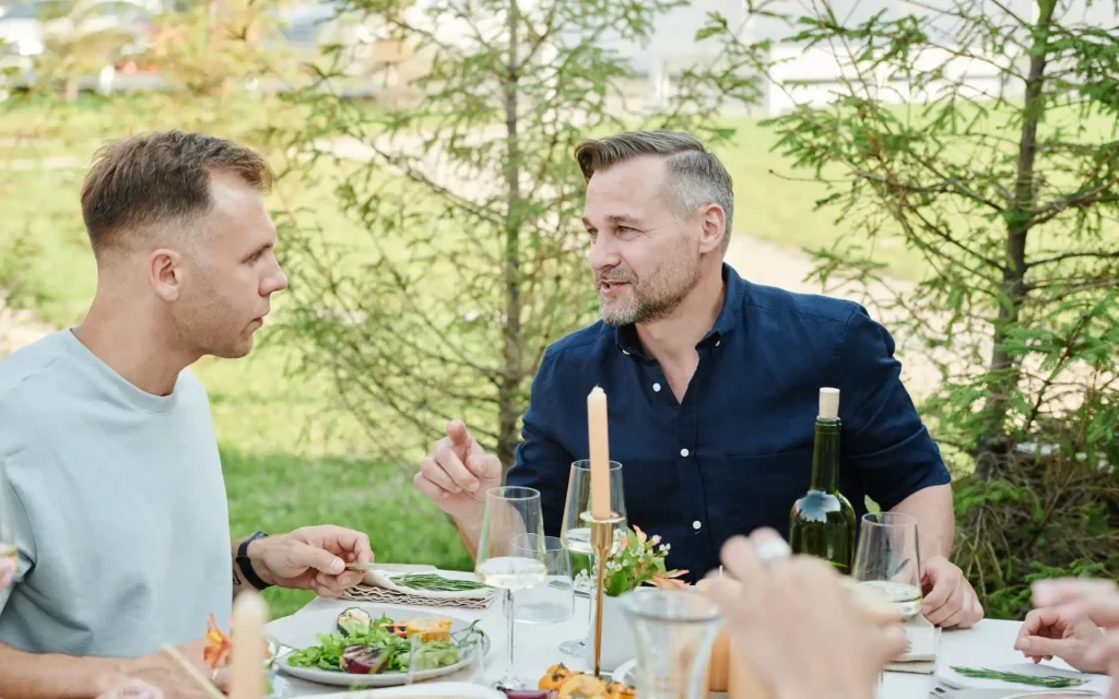 Zwei Männer unterhalten sich bei einem gemeinsamen Essen im Garten.