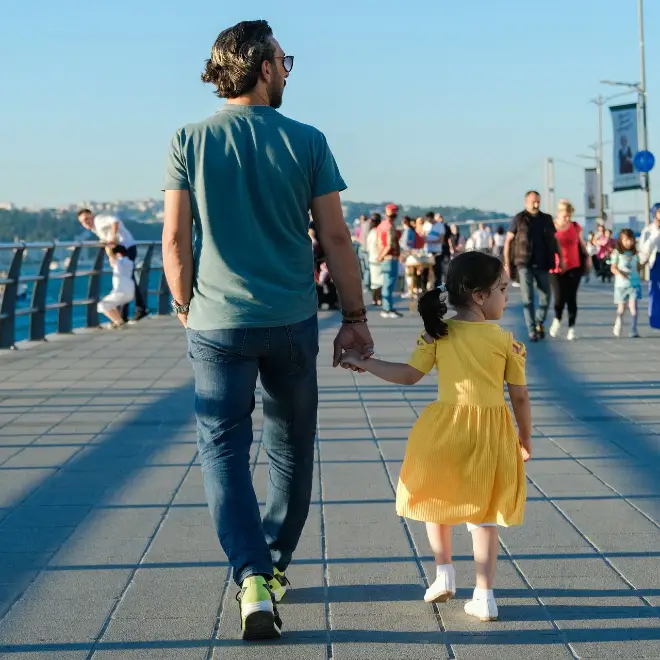 Vater und junge Tochter gehen Hand in Hand über eine Promenade.